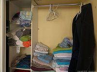 Closet shelves with folded and rolled towels, pillowcases, robe and hangers