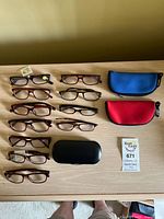 All eleven eyeglasses and three cases on tabletop
