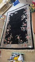Full view of rectangular black rug with floral border and fringe