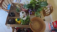 Overview of entire lot on table showing decor pieces, faux plants, glass vases, baskets and thermometer packaging