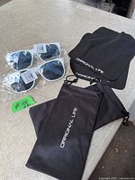 Two packaged white sunglasses, two cloths, two pouches on table