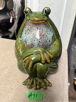 front view of glazed ceramic seated frog figurine showing crossed arms and speckled chest