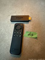 Amazon Fire TV Stick dongle and remote laid on surface, green tape with lot number visible