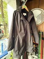 Front view of black hooded coat on hanger showing zipper and pockets
