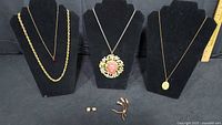 Overview of four necklaces on displays, brooch and earrings laid below