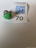 Ring upright beside lot number card showing triangular green turquoise stone and silver bead accents