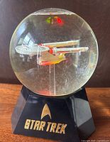 Front view of snow globe showing USS Enterprise model, snow flakes, base with Star Trek logo