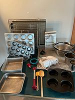 Overview of lot: cooling racks, muffin pans, cookie press, hand mixer, mixing bowls, utensils