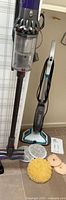 Dyson V10 vacuum on wall mount beside Bissell SpinWave cleaner with pads and manual on floor