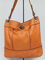 Front view of orange Fossil leather bag showing turn-lock and panel seams