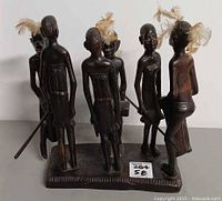 Front view showing six carved figures with feathers, sticks, rectangular base