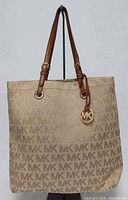 Front view of beige MK monogram tote with handles and charm visible