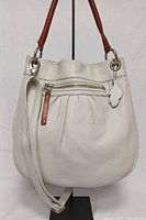 Front view of ivory Roots Olivia leather bag showing shape, hardware, zip pocket, logo fob