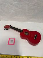 Angled view of red Mahalo NdJ-30RD ukulele lying flat with measuring tape