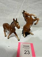Both brown glazed ceramic horse figurines—one rearing, one standing—side by side for scale and comparison