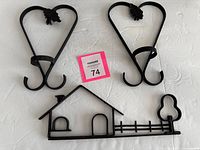 All three wrought iron wall pieces laid out: two heart-shaped hangers and one house-fence silhouette