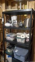 Full view of 5-tier black plastic shelving unit with contents for scale