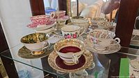 Front view of assorted teacup and saucer pairs on glass shelf