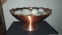 Side view of copper pedestal bowl filled with white marble eggs