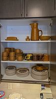 Cupboard view showing majority of Canterbury plates, bowls, mugs and coffee pot