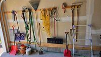 Wall-mounted garden tools including shovels, rakes, hose, extension cord, plant pot and sprinkler