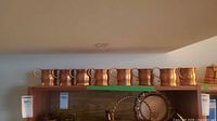 Eight copper mugs lined on shelf