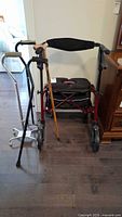 Overall lot showing red neXus forearm rollator with wooden cane and silver quad cane