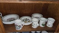 Plates, bowl and four mugs on cabinet shelf