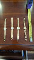 Five gold-tone wristwatches laid out on surface