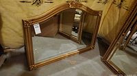 Full view of gold-tone arched wall mirror standing on floor