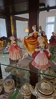 Three Royal Doulton figurines on glass shelf