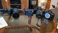 Four cameras displayed on glass table: Sony DSC-F828, Sony Cybershot, Nikon F65, Canon EOS with lens