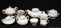 Group shot of nine porcelain pieces: sugar bowls, creamer, teapot, footed bowl