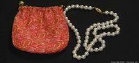 Necklace coiled beside red paisley pouch, showing beads and clasp