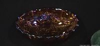 Oblique view of iridescent amber carnival glass bowl showing scalloped rim and iridescence