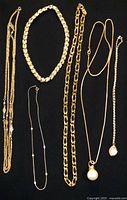All six gold-tone necklaces laid out on dark background