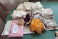 Overview of folded vintage lace linens and packaged tablecloth on table