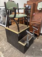 Full view of shoe shine stand showing base, drawers, metal footrests, and green upholstered chair