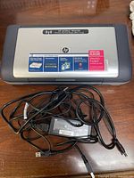 Closed HP OfficeJet H470 printer with power adapter and USB cable displayed