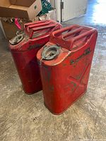 Front angled view of both red steel jerry cans showing paint wear, dents, caps present