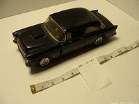 Full view of black 1955 Chevy diecast model beside tape for scale
