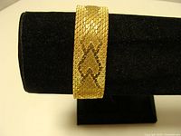 Front view of wide gold-tone bracelet on display stand