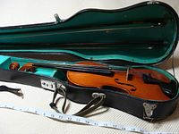 Violin inside open case with two bows and tape for scale