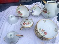 Full tea set shown: teapot, creamer, sugar, cups and stack of saucers displaying fruit motif and gold trim