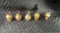 Front view of five miniature cloisonné vases on quilted backdrop, interiors visible
