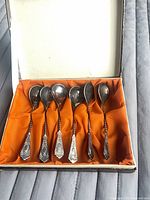 Open box showing six ornate silverplate teaspoons in orange satin lining