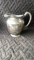 Front view of sterling silver water pitcher showing bulbous body, foot, spout, handle, tarnish