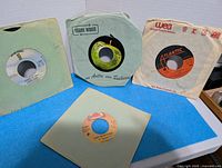 Four 45 RPM records in sleeves standing and lying on table