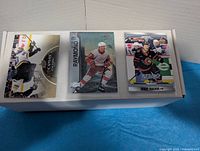White storage box with three example hockey cards on top: UD Canvas Penguins player, Lucas Raymond Red Wings, Brady Tkachuk Senators