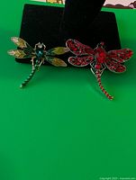 Two rhinestone dragonfly brooches on display